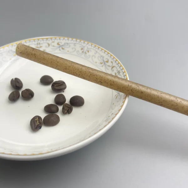 Close-up view of a coffee grounds straw placed over a decorative plate with scattered coffee beans, showcasing its eco-friendly composition.